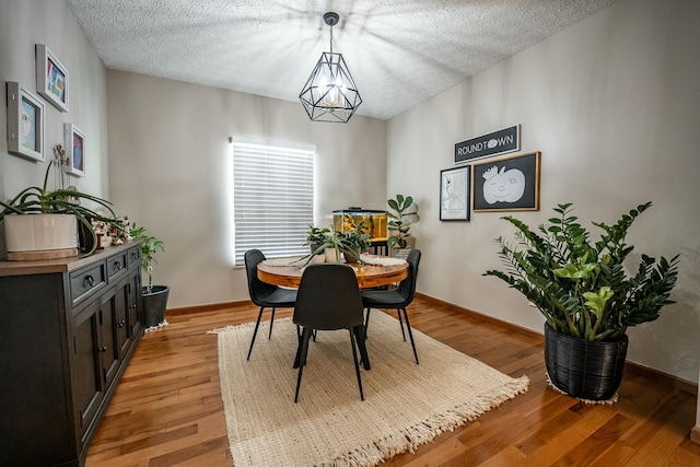 dining space with light wood-type flooring, a textured ceiling, and an inviting chandelier