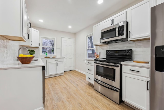 kitchen with tasteful backsplash, white cabinetry, stainless steel appliances, and light hardwood / wood-style flooring