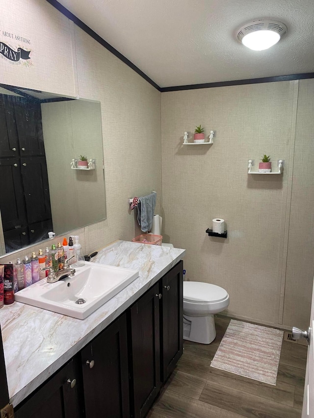 bathroom with ornamental molding, vanity, a textured ceiling, hardwood / wood-style floors, and toilet