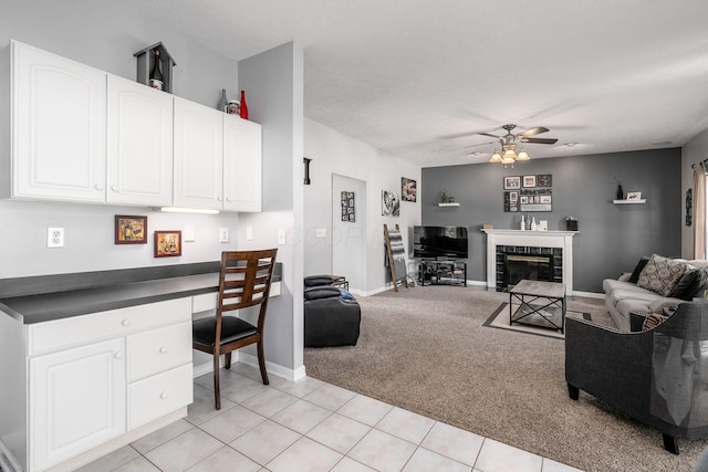 carpeted living room with ceiling fan, built in desk, and a textured ceiling