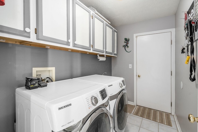 washroom with washing machine and clothes dryer, light tile patterned floors, cabinets, and a textured ceiling