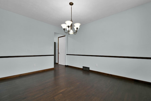 empty room with a chandelier and dark wood-type flooring