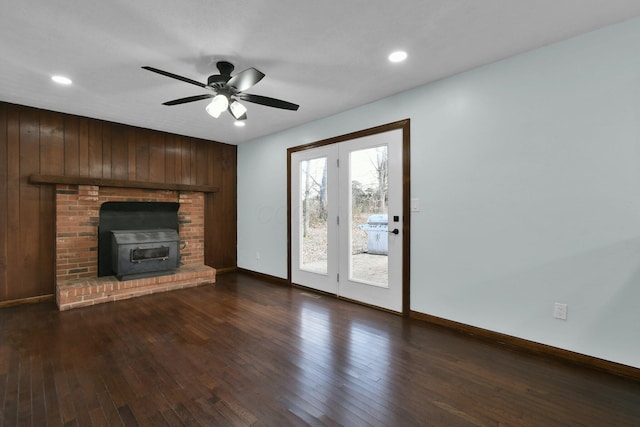 unfurnished living room with ceiling fan, wood walls, and dark wood-type flooring