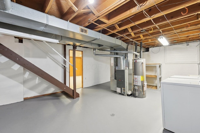 basement featuring washing machine and clothes dryer, heating unit, and water heater