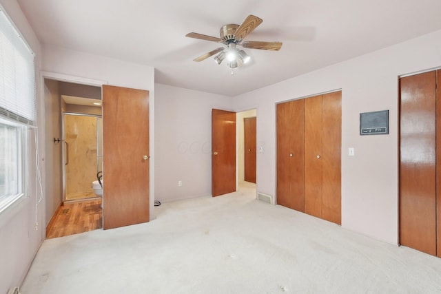 carpeted bedroom featuring ensuite bath, ceiling fan, and two closets