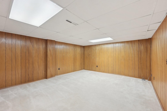 basement with a paneled ceiling, wooden walls, and light colored carpet