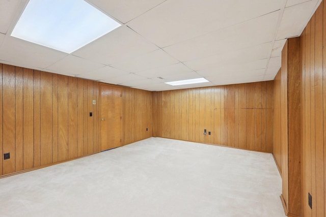 basement featuring a paneled ceiling, wood walls, and light colored carpet