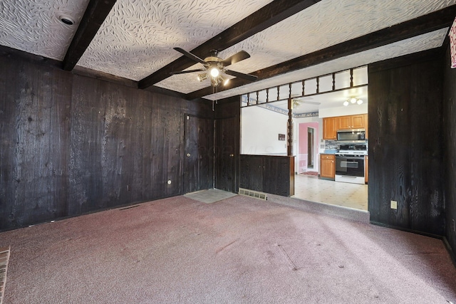 carpeted spare room with beam ceiling, wooden walls, ceiling fan, and a textured ceiling