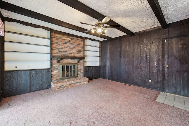 unfurnished living room with ceiling fan, built in features, beamed ceiling, a textured ceiling, and wooden walls