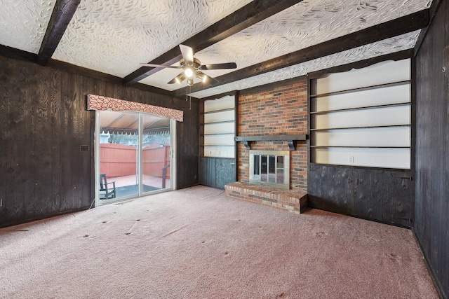 unfurnished living room with ceiling fan, built in features, beamed ceiling, wood walls, and a textured ceiling