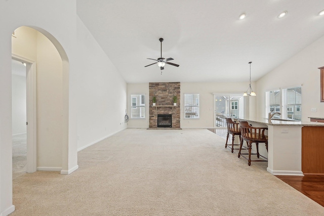 living room with ceiling fan with notable chandelier, lofted ceiling, light carpet, and a fireplace