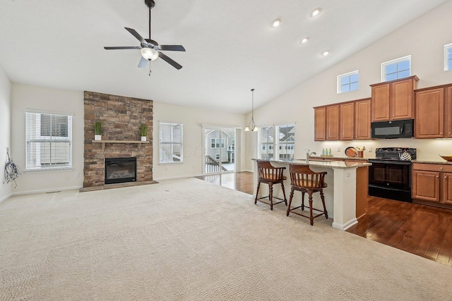 kitchen featuring pendant lighting, black appliances, a kitchen island with sink, a fireplace, and a kitchen breakfast bar