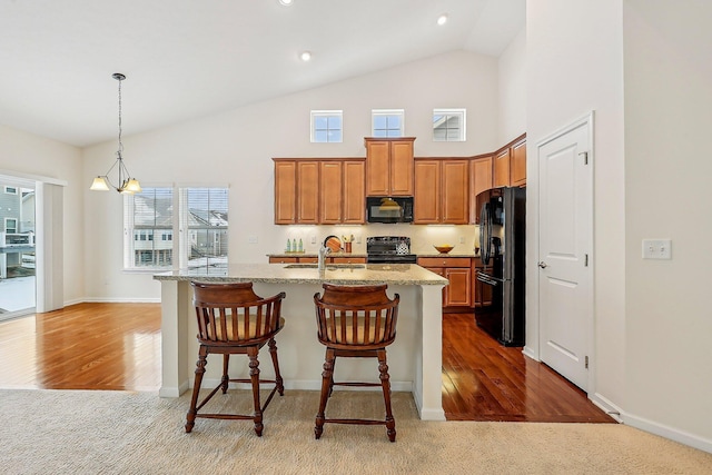 kitchen with a center island with sink, a notable chandelier, a breakfast bar, black appliances, and sink