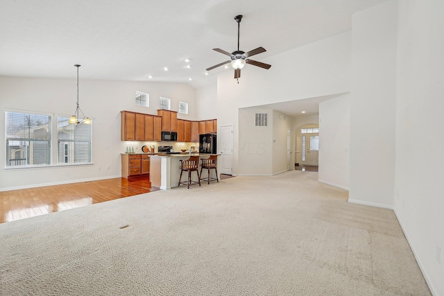 kitchen with a kitchen breakfast bar, a center island with sink, black appliances, hanging light fixtures, and ceiling fan