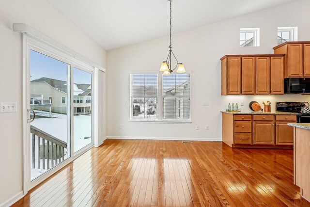 kitchen with hardwood / wood-style floors, black appliances, hanging light fixtures, an inviting chandelier, and lofted ceiling