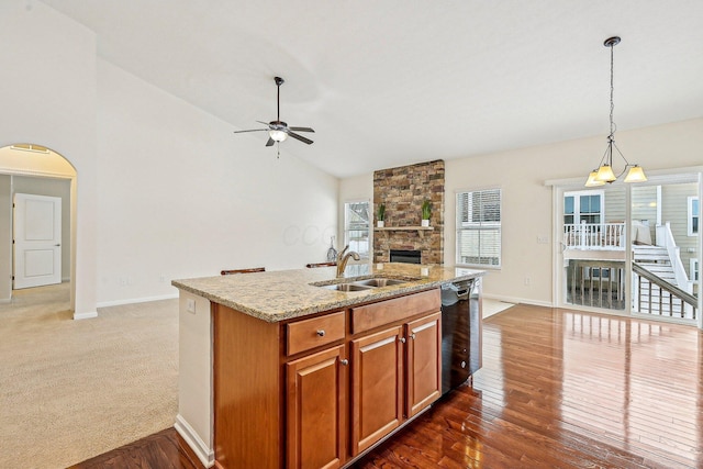 kitchen with light stone counters, decorative light fixtures, a kitchen island with sink, black dishwasher, and sink