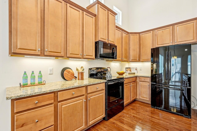 kitchen featuring light stone counters, light wood-type flooring, and black appliances