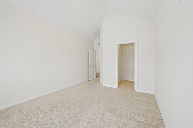 unfurnished bedroom with lofted ceiling, a closet, a spacious closet, and light carpet