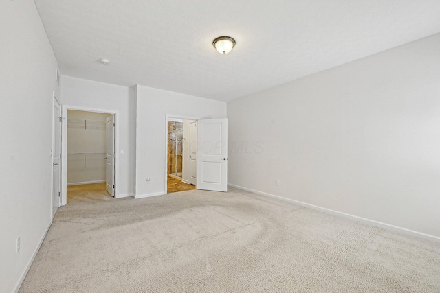 unfurnished bedroom with light colored carpet, a closet, and a spacious closet