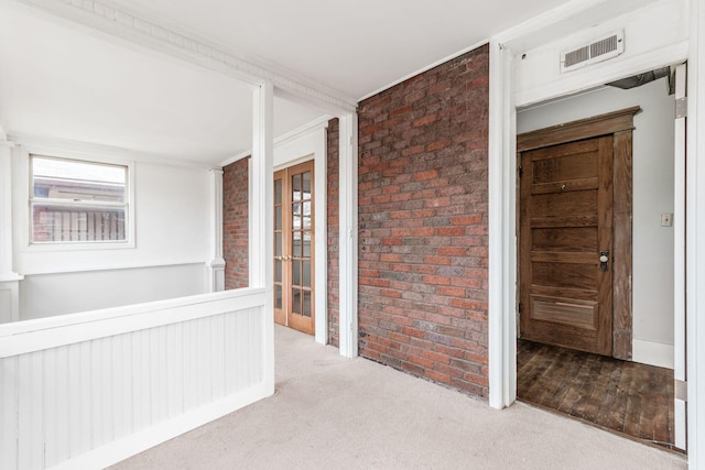 hallway featuring crown molding, light colored carpet, and brick wall