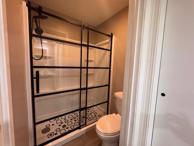 bathroom featuring toilet, wood-type flooring, and a shower with door