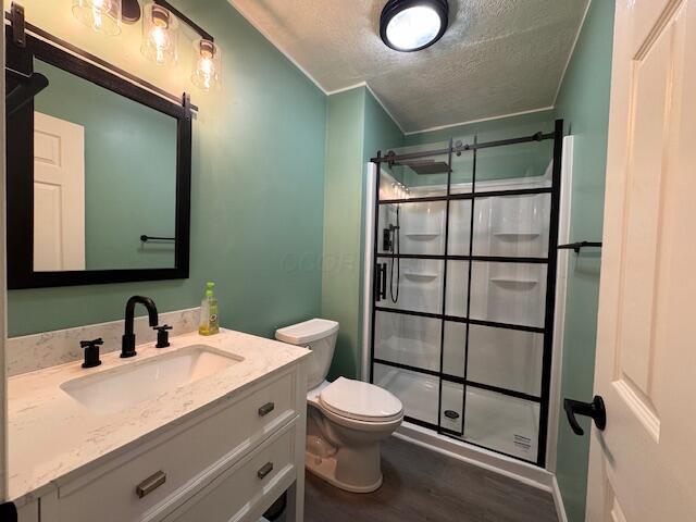 bathroom with vanity, hardwood / wood-style flooring, toilet, a textured ceiling, and a shower with shower door