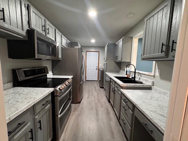 kitchen featuring appliances with stainless steel finishes, light stone counters, gray cabinetry, sink, and light hardwood / wood-style flooring