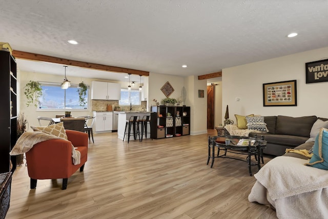 living room with beam ceiling, sink, and light hardwood / wood-style floors