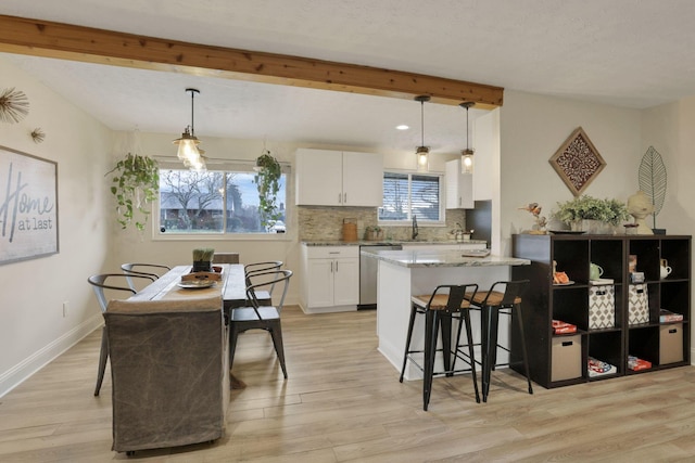 kitchen featuring light stone countertops, dishwasher, white cabinets, and decorative light fixtures