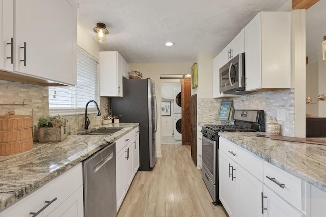 kitchen with stainless steel appliances, white cabinetry, stacked washer and clothes dryer, and sink