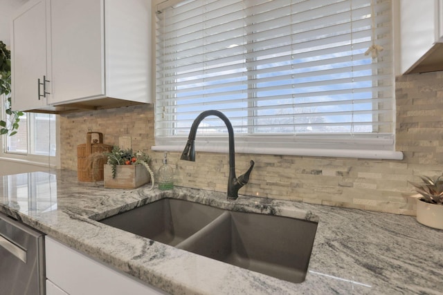 kitchen featuring a healthy amount of sunlight, light stone countertops, white cabinetry, and sink