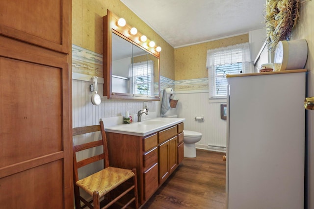 bathroom featuring baseboard heating, wood walls, hardwood / wood-style floors, toilet, and vanity