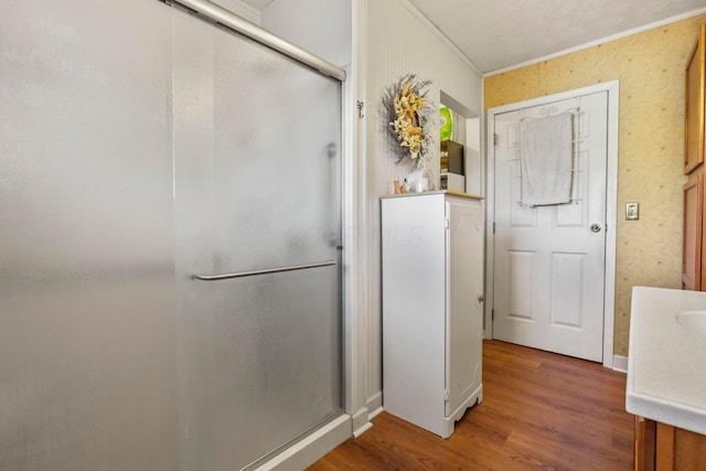 bathroom featuring hardwood / wood-style floors, vanity, a shower with door, and crown molding