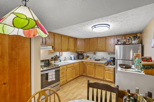 kitchen with backsplash, a textured ceiling, stainless steel appliances, light hardwood / wood-style floors, and hanging light fixtures