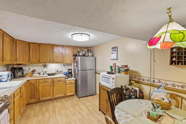 kitchen with appliances with stainless steel finishes, light wood-type flooring, backsplash, a textured ceiling, and pendant lighting