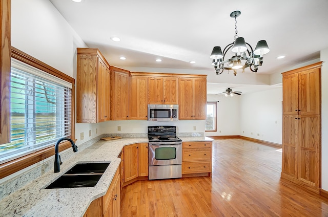 kitchen with light wood-type flooring, ceiling fan with notable chandelier, stainless steel appliances, sink, and hanging light fixtures