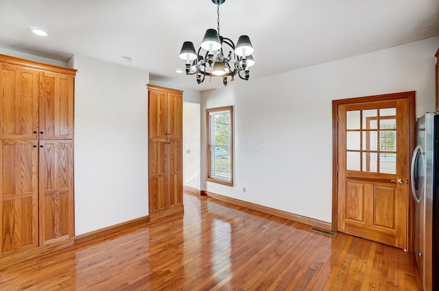 unfurnished dining area featuring an inviting chandelier, a wealth of natural light, and light hardwood / wood-style flooring