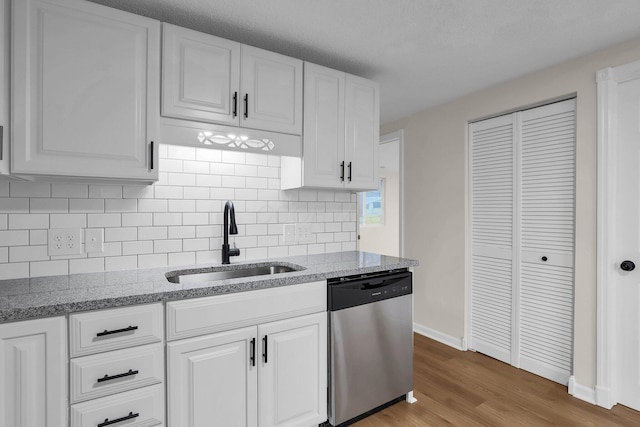 kitchen with sink, light hardwood / wood-style flooring, stainless steel dishwasher, decorative backsplash, and white cabinetry