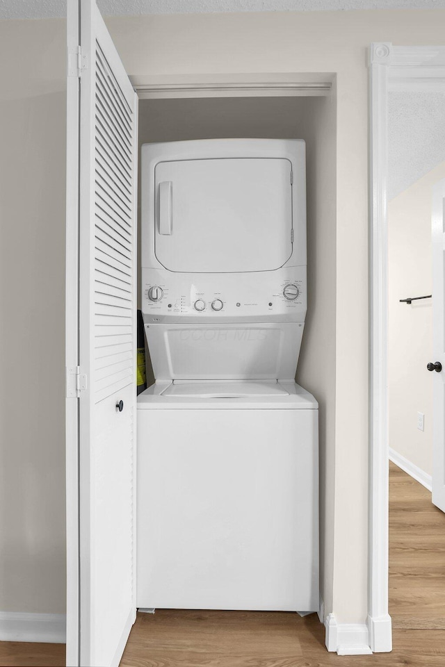 laundry area with wood-type flooring, a textured ceiling, and stacked washer / dryer