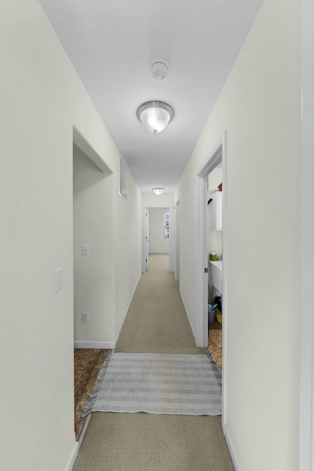 corridor with a textured ceiling and light colored carpet