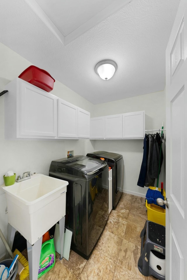 laundry area featuring cabinets, sink, washer and dryer, and a textured ceiling