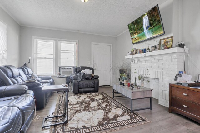 living room featuring a brick fireplace, cooling unit, light hardwood / wood-style floors, a textured ceiling, and ornamental molding