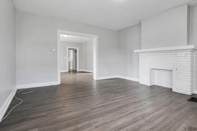 unfurnished living room featuring a textured ceiling, dark wood-type flooring, and a brick fireplace