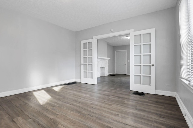 empty room with a fireplace, french doors, dark wood-type flooring, and a textured ceiling