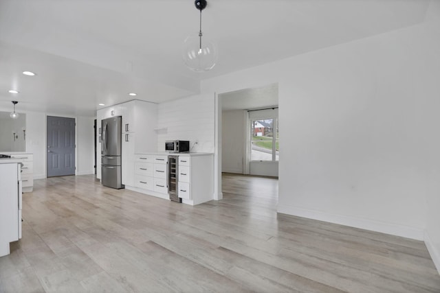 interior space with white cabinets, light hardwood / wood-style floors, wine cooler, hanging light fixtures, and stainless steel refrigerator