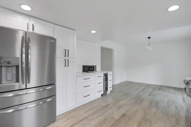 kitchen featuring hanging light fixtures, white cabinets, stainless steel appliances, and light hardwood / wood-style flooring