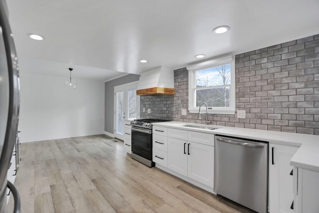 kitchen with white cabinetry, sink, pendant lighting, custom range hood, and appliances with stainless steel finishes