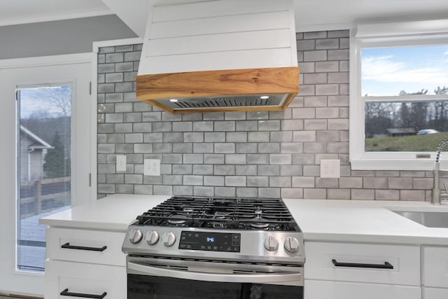 kitchen with decorative backsplash, premium range hood, stainless steel gas range oven, sink, and white cabinetry