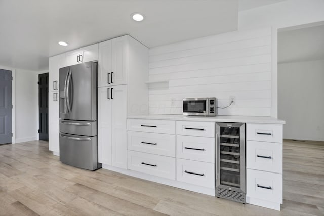 kitchen featuring wine cooler, white cabinets, light wood-type flooring, and appliances with stainless steel finishes