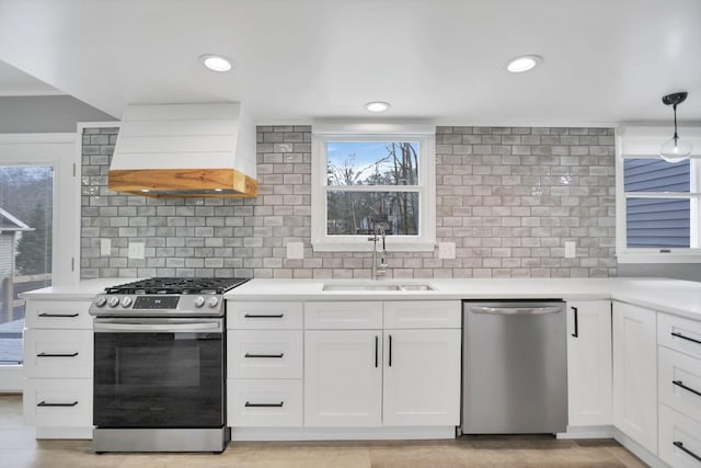 kitchen with custom exhaust hood, stainless steel appliances, sink, decorative light fixtures, and white cabinetry